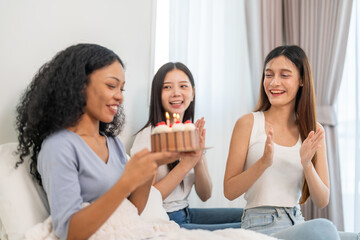 Multicultural group of women friends happy surprising friend with birthday cake at joyful party, celebration of friendship and happiness, happy birthday, candles, smiles, gift and fun at home