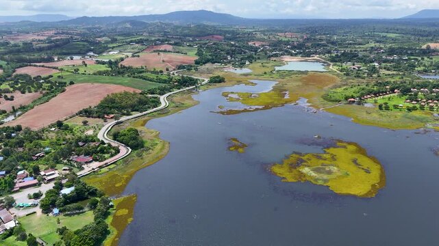 Drone footage of aerial view of Lam Phra Phloeng reservoir and surrounding farmland in Wang Nam Khiao, Nakhon ratchasima, Thailand. Scenic landscape of countryside with curved rural roads 