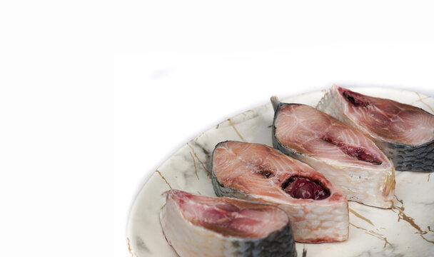 Raw Pieces of fresh tenualosa ilisha or hilsa fish in the white plate on white background. Very famous traditional fish among Bengali's in India, it also national fish of India.