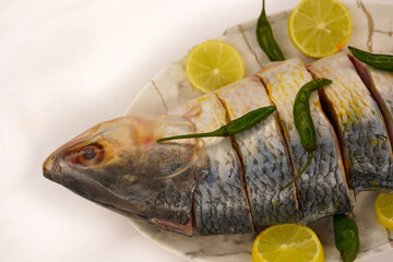 Indian fish fry recipe- fresh whole Hilsa fish or Ilish fish or Poplet cut into slices. cleaned and ready for frying along with spices. ingredients and recipe, white background with copy space.