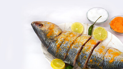 Indian fish fry recipe- fresh whole Hilsa fish or Ilish fish or Poplet cut into slices. cleaned and ready for frying along with spices. ingredients and recipe, white background with copy space.
