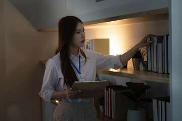 Organized Workspace. Young woman arranging books in modern office at night.