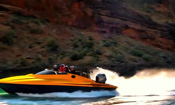 A yellow and black speedboat in motion, creating a splash of water as it moves. In the background, there is a rocky hillside, suggesting that the boat is navigating through a river or canyon area.