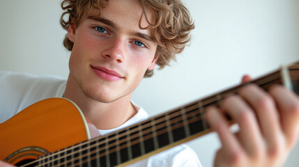 Close-up of a young man with a broad face, light skin, and friendly blue eyes, dressed in a musician's attire, playing a guitar. 