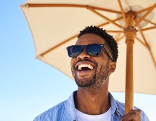 Happy African American man enjoying sunny day at the beach under large white umbrella wearing black sunglasses and a white shirt