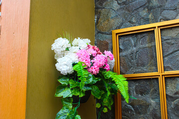 Decorative pot of vibrant pink and white artificial flowers with green foliage next to a golden window frame