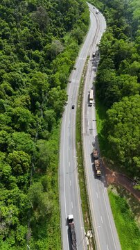 Vertical video aerial view of curvy road highway number 304 through dense forest in Thailand