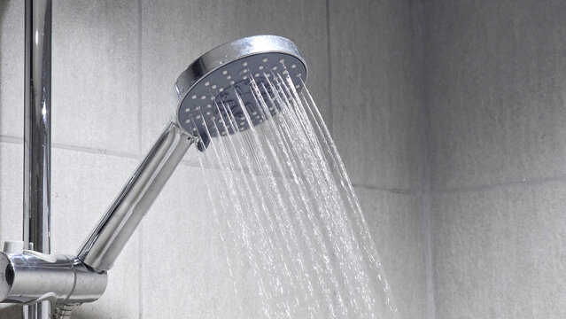 Running shower head in tiled bathroom wall.