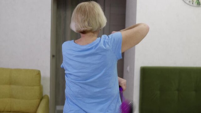 Mature woman alleviating back itching tapping with specialized assistive device, showcasing independent self care and personal wellness during daily home routine