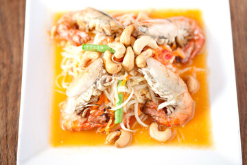 Som tam Thai with river prawns and roasted cashew nuts served on a white plate, presenting authentic street food and vibrant flavors.