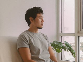 Side view of Thai man sitting by window with thoughtful gaze in peaceful white interior
