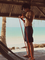 Man exercise and workout with rubber band in the hut by the sea. Beach relaxed vibe.