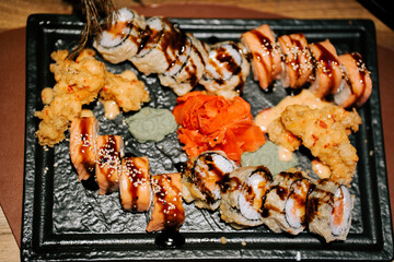 Sushi platter featuring various rolls and garnishes served on a black stone plate