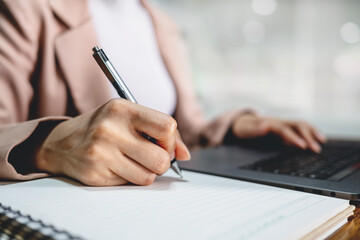 Company employee writing on notebook with working on laptop computer in office. Business planning concept