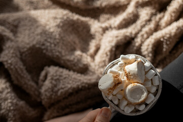 Woman holding mug with hot chocolate, marshmallows and roasted meringue on cozy blanket background...