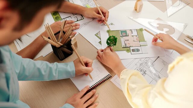 Architect and engineer use tree model discuss about building blueprint on table with architectural document, measurement tools and wooden block scatter around at modern office. Closeup. Delineation.