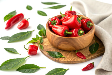 Red peppers in wooden bowl with green leaves on clean white background