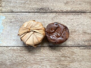Two pieces of coconut palm sugar (Gula Melaka) on a rustic wooden surface. One piece is...