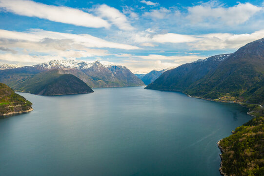 Majestic Hardanger fjord with deep tranquil waters stretches to horizon among mountains covered with snow. Higher peaks under overcast sky in Norway