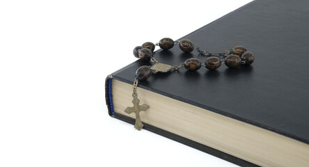 Rosary placed on top of black Bible isolated on white