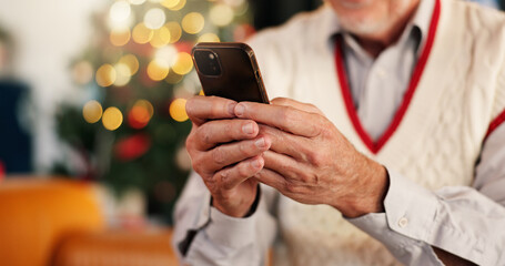 Hands, person and phone for Christmas at house with social media, browsing internet or gift search. Senior man, bokeh and typing on app for xmas message, online shopping and update of festive season