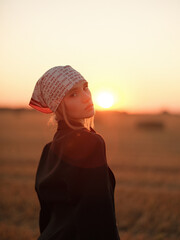 Portrait of young blonde woman in bandana and black jacket, posing on meadow at sunset.