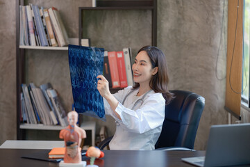 An Asian female doctor holding and checking a lung x-ray film at a hospital.