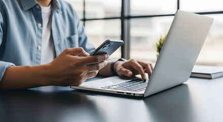 Focused young man working on laptop and using smartphone, multitasking and productivity concept