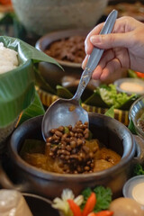Indonesian sambal goreng krecek, a spicy stew of cow skin and beans, served with kacang tolo in a traditional earthenware pot.