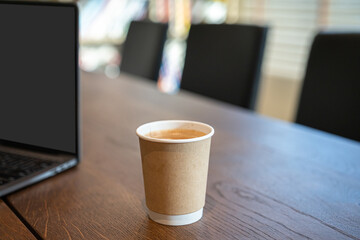 Close-up of Hot coffee latte with latte art milk foam in cup made of paper and laptop computer on...