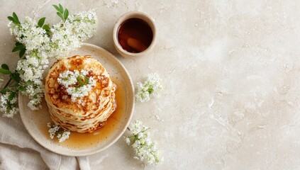 Stacked pancakes, drizzled with syrup, surrounded by white flowers on a light beige surface
