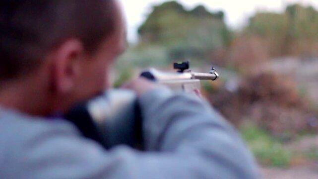 A young man aims a rifle with intense focus, blurring into the background&mdash;capturing tension, precision, and the still concentration of a critical moment.