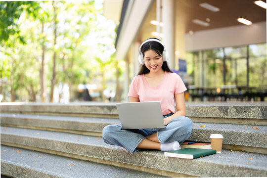 Concept of e-learning, distance study or remote learning concept, Young happy  school girl , college or university student with textbook  and headphones using laptop sitting outdoor at stair.