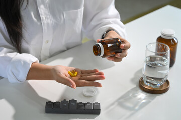 Woman taking dietary supplements with water and a weekly pill organizer on the table. Health care...