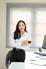 Confident businesswoman holding a cup of coffee standing confidently in a modern office
