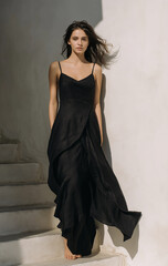 A minimalist black linen dress with a loose fit, the model poses on a street in Greece for a brand photoshoot.