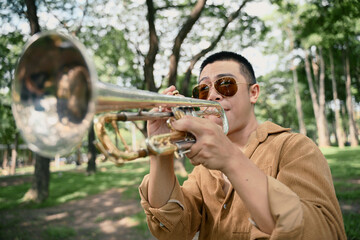 Dynamic close up of trumpet player in sunglasses performing outdoors in a sunny green park
