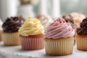 Assorted colorful cupcakes with swirled frosting in pink yellow and chocolate flavors on counter