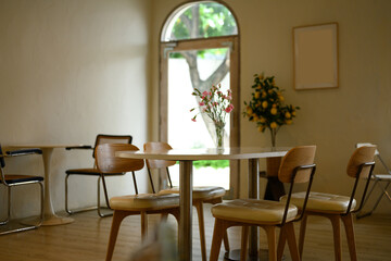 Cozy and minimalistic cafe interior with wooden chairs and a round table decorated with a vase of...