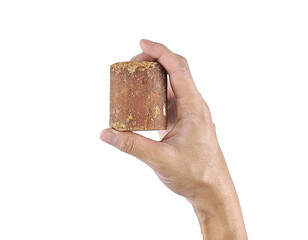 Close-up of human hand gripping brown jaggery, used in Asian and tropical cooking