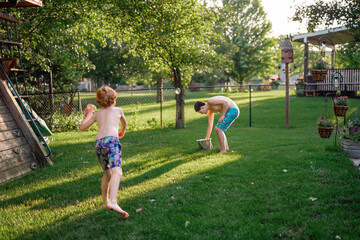 Two boys having summer water fight in green backyard