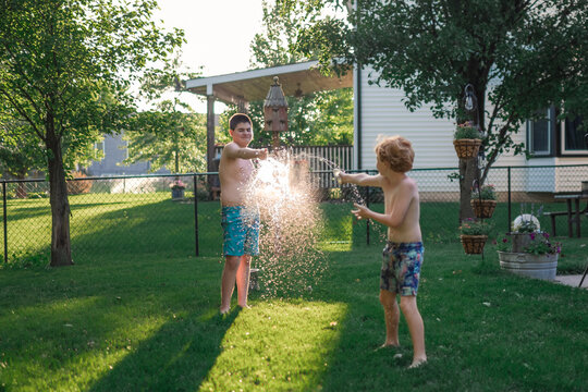 Two boys having summer water fight in green backyard