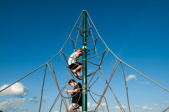 Two boys climbing rope structure under clear summer blue sky