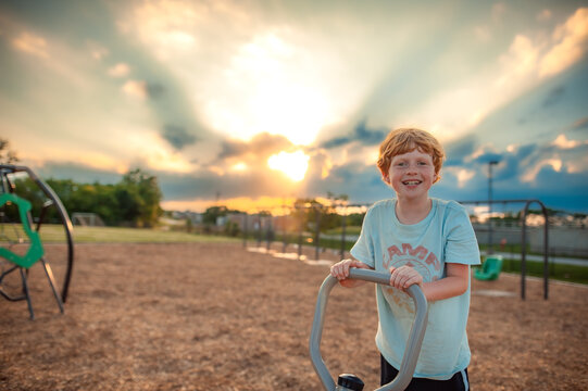 Redheaded boy plays outdoors on playground at golden sunset
