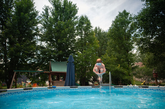 Young boy cannonballs into backyard pool on sunny day