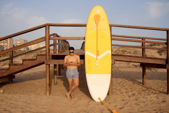 Tourist using smartphone on beach with paddle board