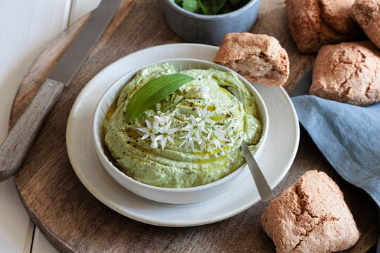 Wild garlic dip with herb cream cheese and bread rolls on a wooden board