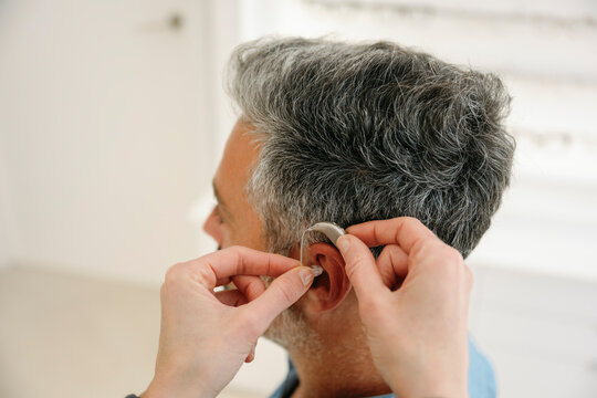 Audiologist assisting client with hearing aid fitting indoors