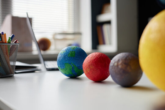 Closeup showing colorful model planets arranged on desk with blurred laptop and office supplies in background, illustrating educational science concept for astronomy learning