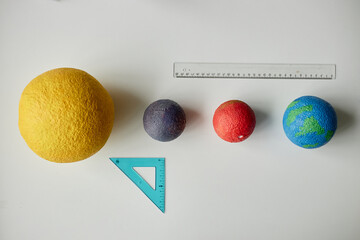 Four spherical educational models representing planets arranged in size order on surface, accompanied by transparent ruler and blue triangular set square for scale comparison © Seventyfour